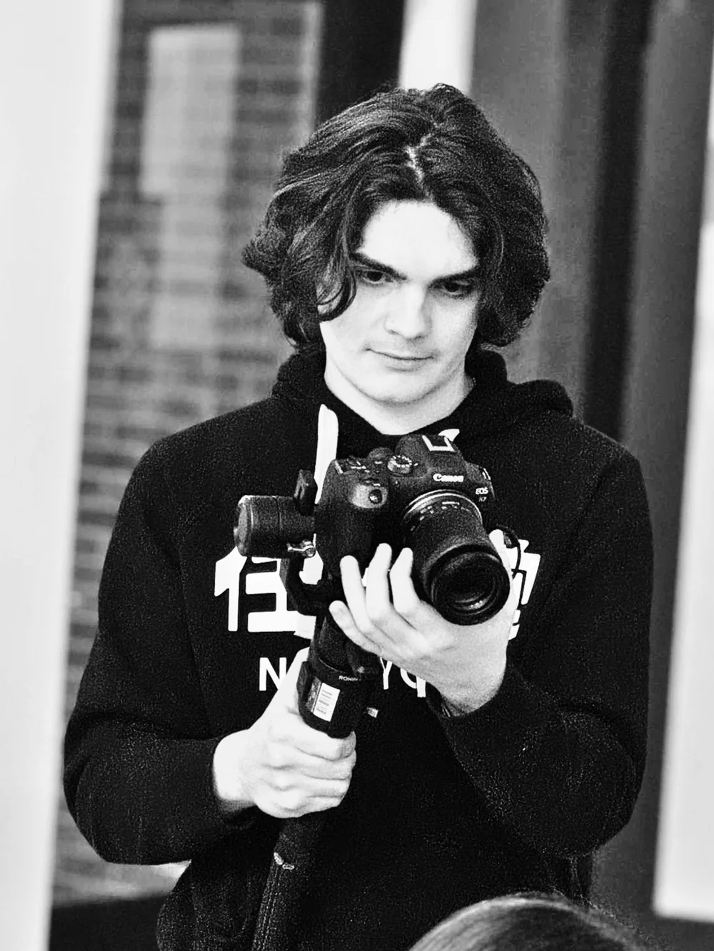 David Hagerstrom in a dark hoodie, holding a Canon DSLR on a gimbal and looking down at the camera